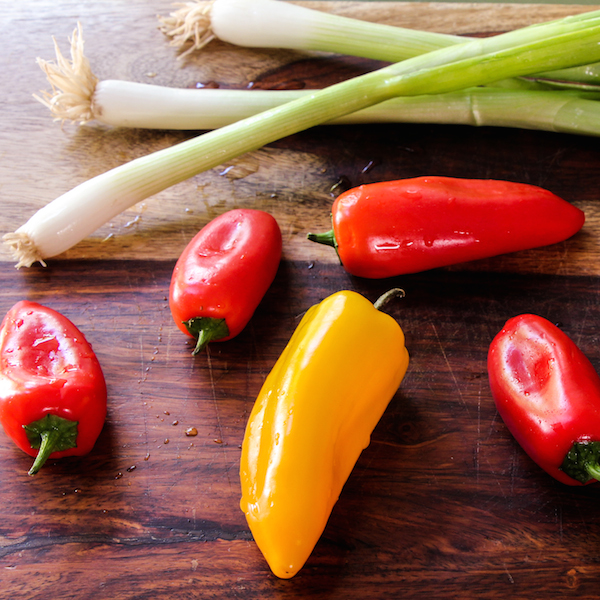 5 mini bell peppers on a cutting board with 3 scallions.