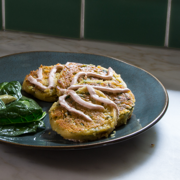 Spinach and chickpea pancakes topped with sriracha yogurt on a plate.