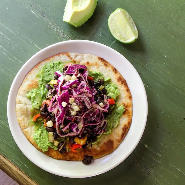 A simple Mexican tostada on a fried flour tortilla, with guacamole, black beans, peppers and a cabbage and corn salad.