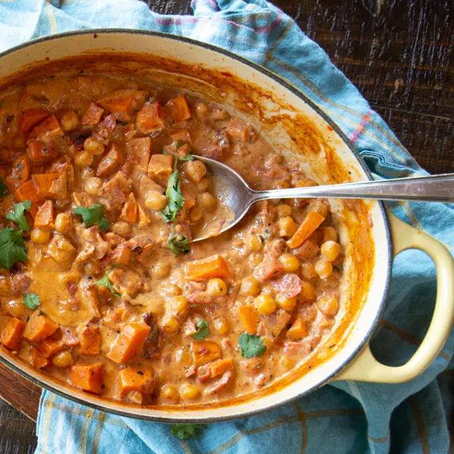 A large pot of sweet potato and chickpea curry, topped with chopped parsley.