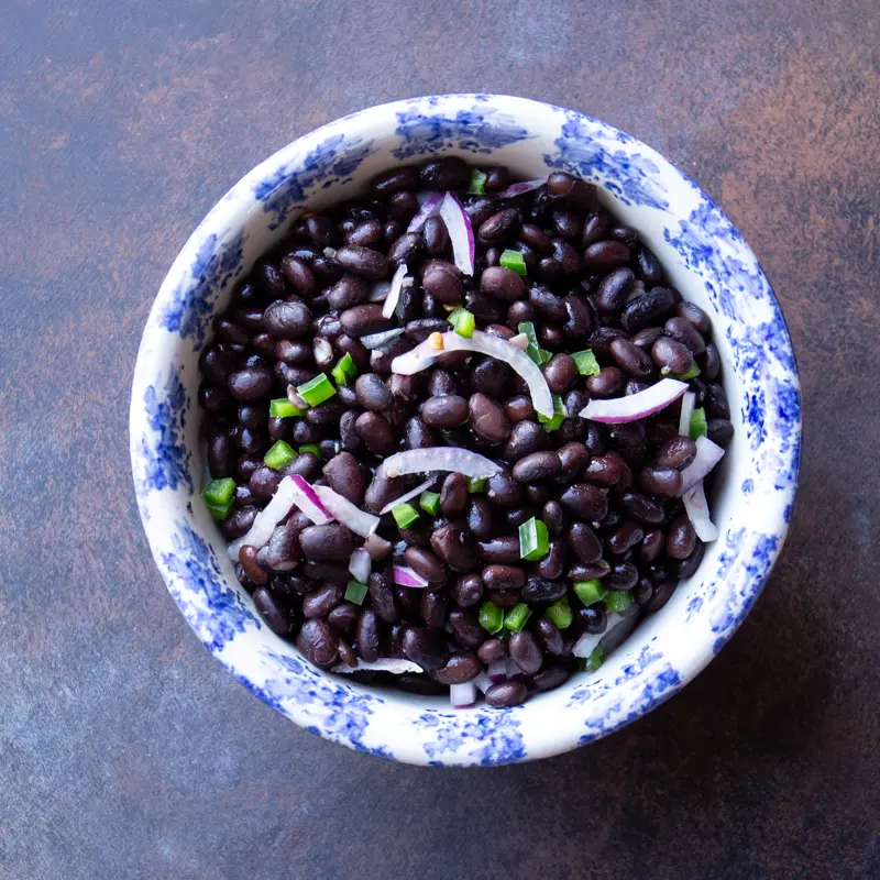 A bowl of cooked black beans with slivers of red onion, and chopped peppers.