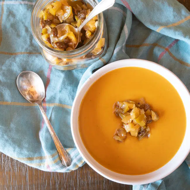 Bowl of roasted butternut squash and sweet potato soup with coconut milk. The soup is topped with apple chutney.