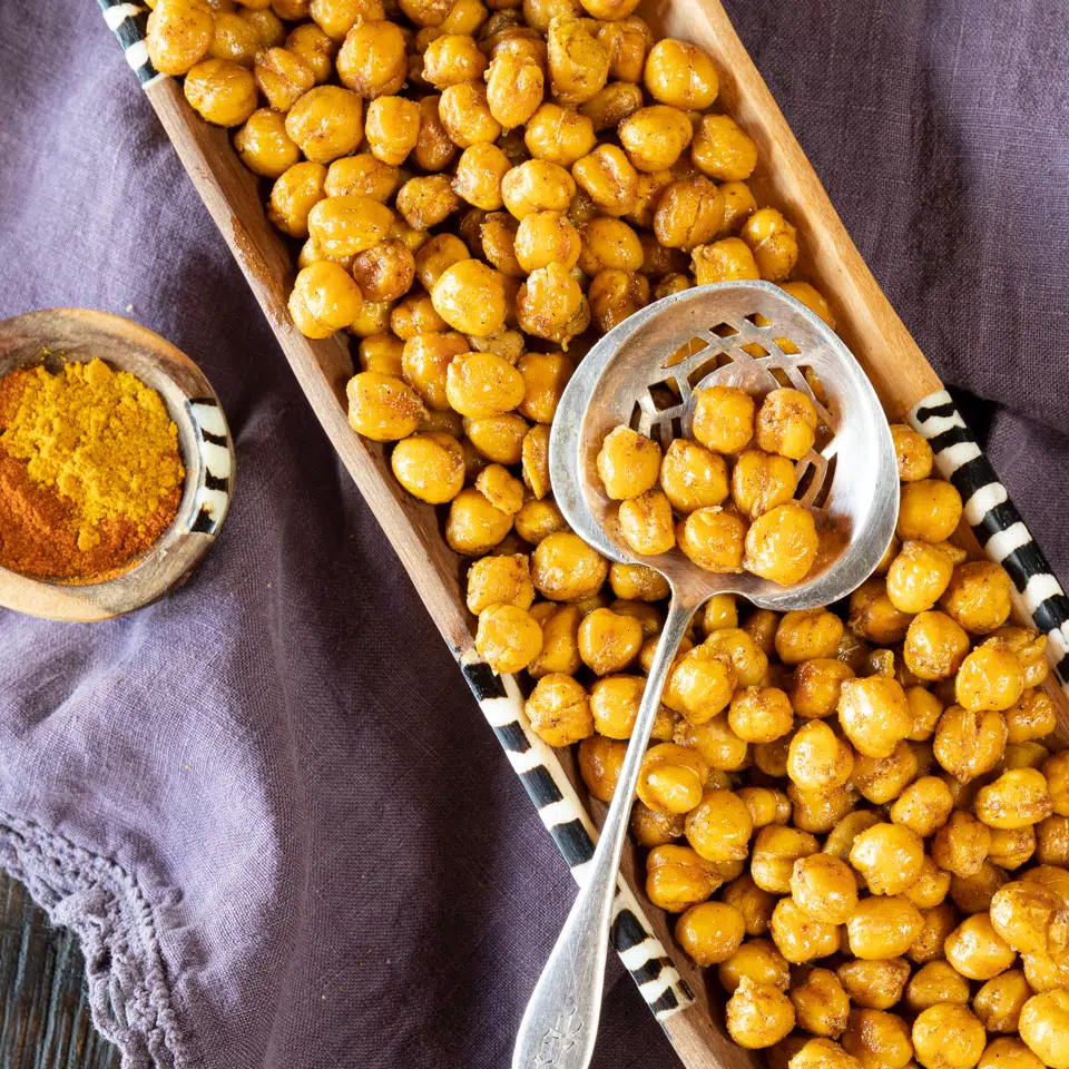 A wooden tray filled with crispy roasted chickpeas that were dusted with curry powder.