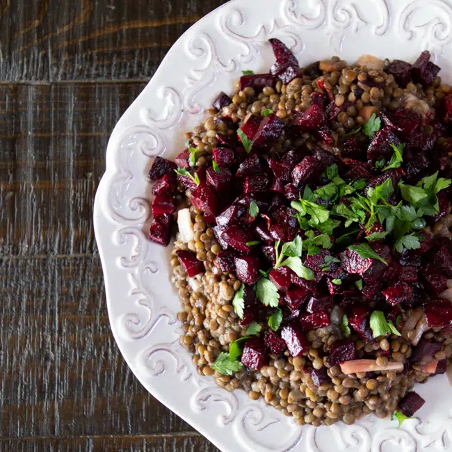 A platter of lentils topped with a pickled beet salad, and topped with parsley.