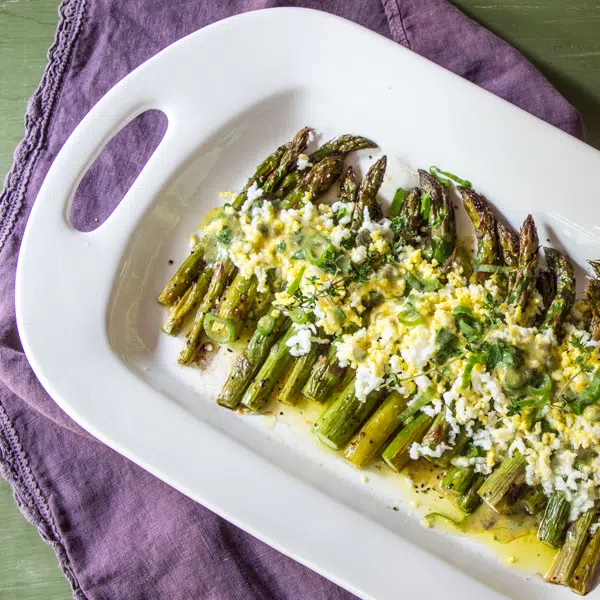 A serving tray of roasted asparagus, topped with a gribiche sauce.