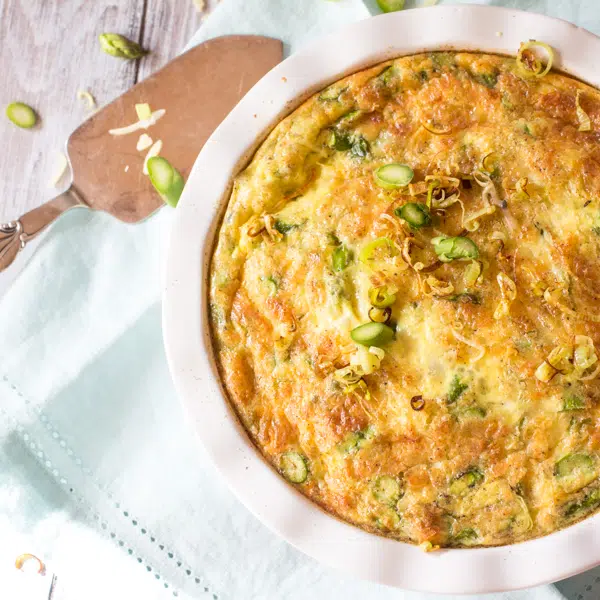 A baking dish filled with an asparagus quiche that's lightened. It has a hash brown crust.