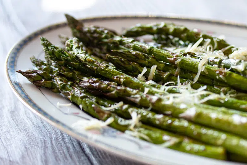 Asparagus spears cooked in the air fryer on a plate, and topped with a little Parmesan cheese.