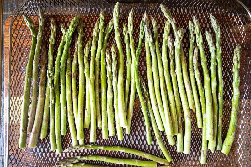 Fresh asparagus in the basket for an air fryer, all spread out and ready to roast.