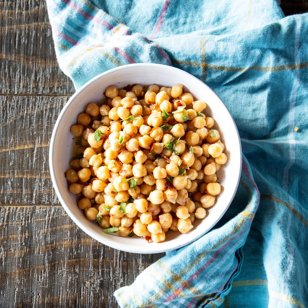 A bowl full of cooked chickpeas, with a few herbs scattered over the top.