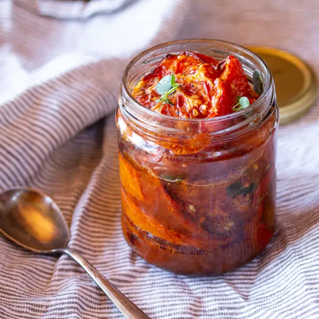 Jar of balsamic roasted tomatoes with a little fresh oregano.