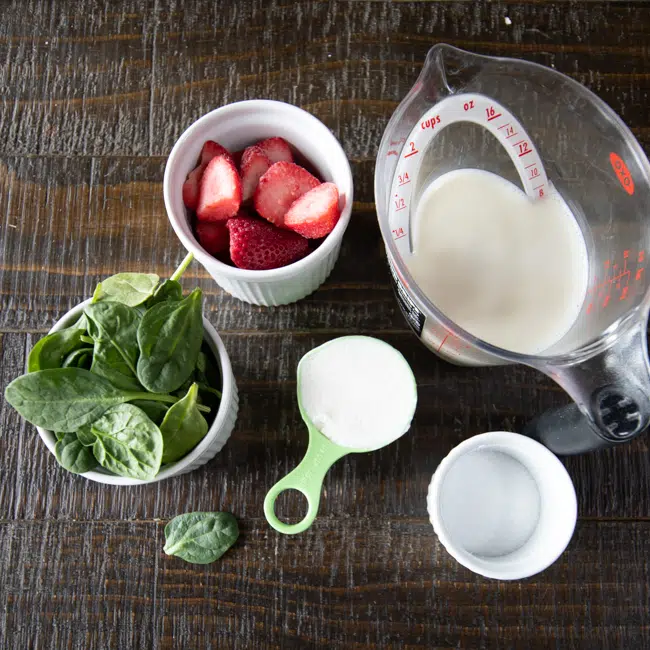All of the ingredients used to make a Spinach and Strawberry Smoothie: spinach, strawberries, oat milk, dairy-free yogurt and monk sugar.