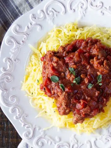 White platter heaped with golden spaghetti squash cooked in the air fryer, and topped with a meatless hearty tomato sauce.
