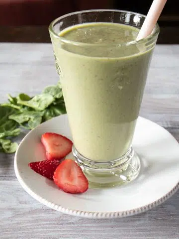Spinach smoothie with strawberries poured into a glass with a straw.