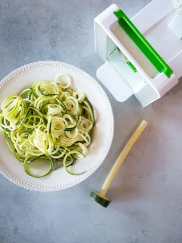 A bowl of spiralized zoodles next to a spiralizer.