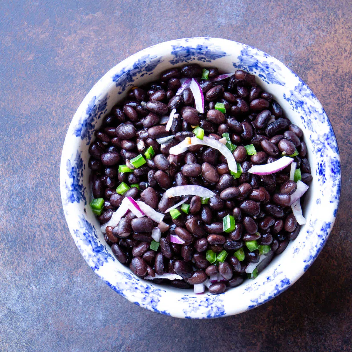 Bowl of black beans with slivers of red onion and minced jalapeño.