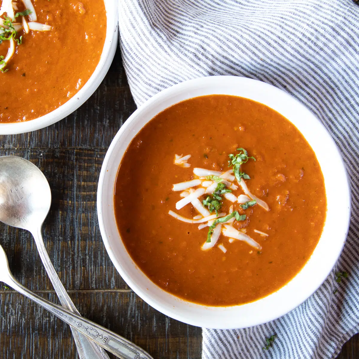 Two bowls of roasted tomato soup topped with a little grated cheese and basil.