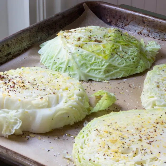 Thick slices of cabbage topped with olive oil, salt and pepper, arranged on a baking sheet.
