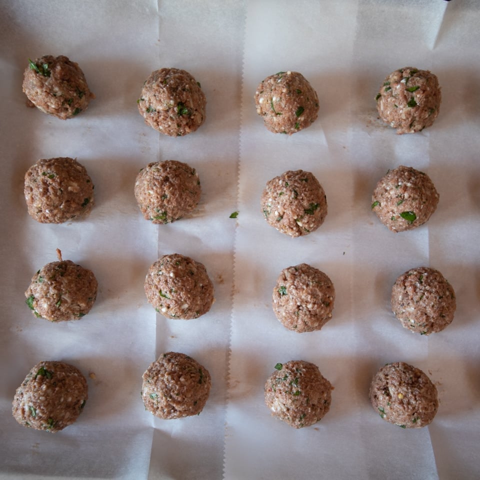 Meatball made with Beyond Beef arranged on a parchment lined baking sheet, ready to go in the oven.