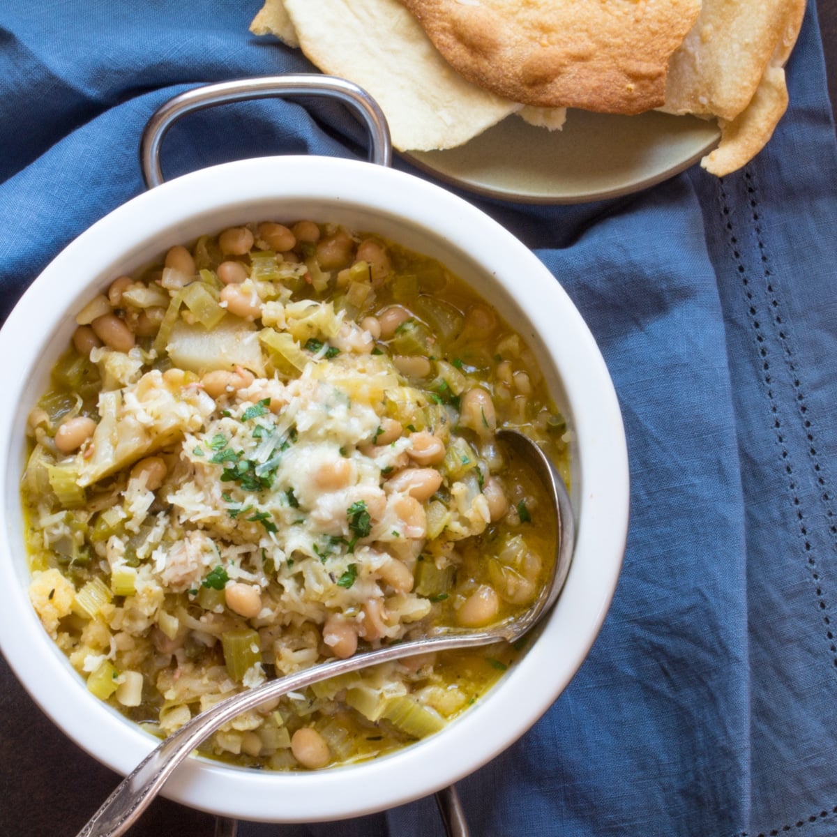 A pot of hearty cauliflower soup with white beans, topped with cheese.