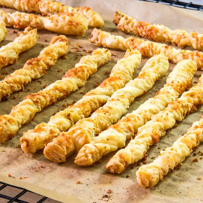 Freshly baked cheese straws made with puff pastry, on a cooling rack.