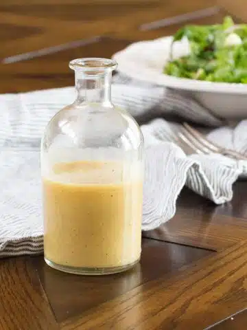 A small bottle of homemade pear vinaigrette, with a green salad in the background.