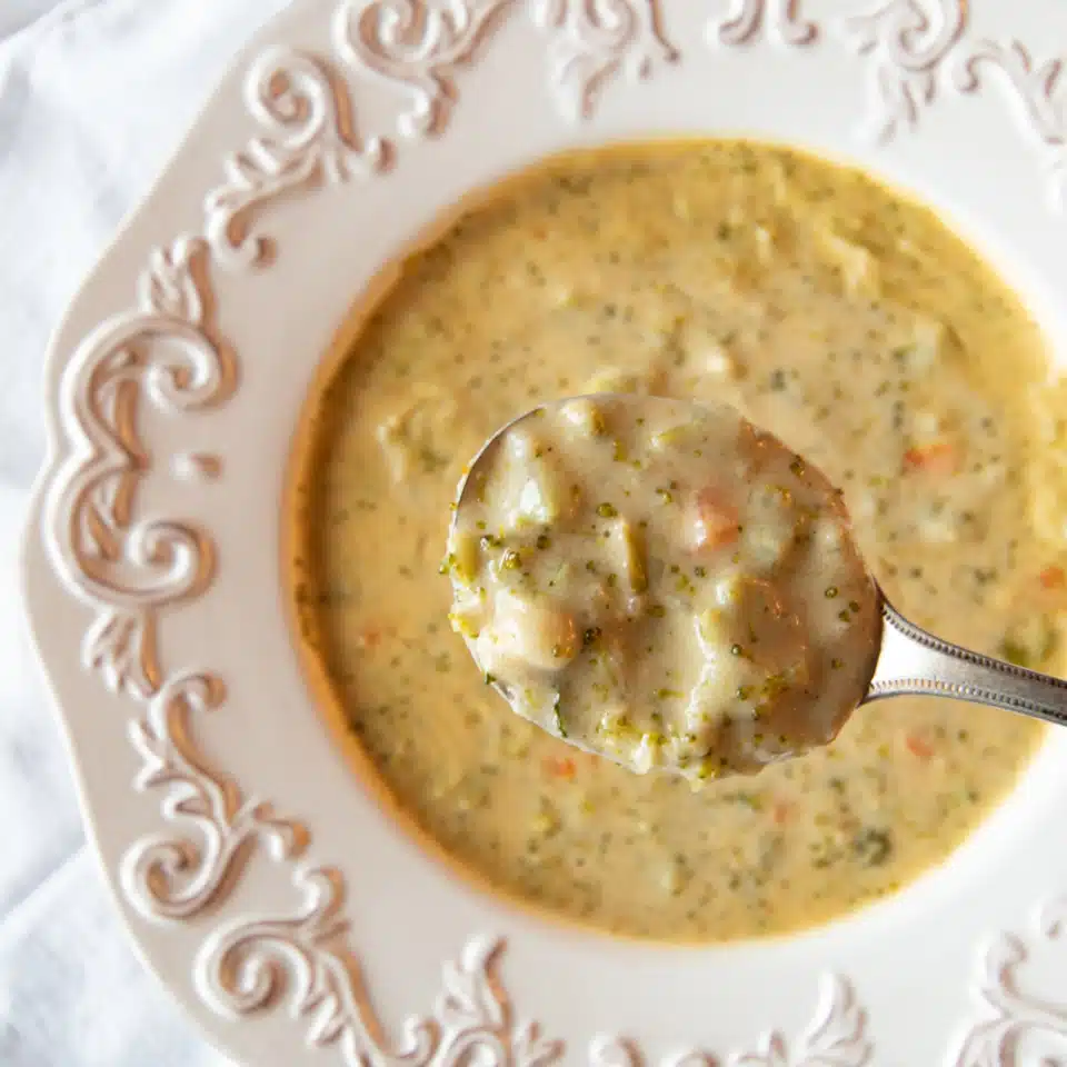 Creamy vegetarian broccoli cheddar soup in a bowl, with a close up of some of the soup in in a soup spoon.