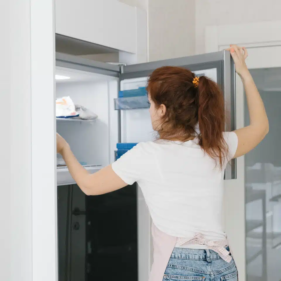 Girl standing in front of open freezer.