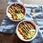 Two bowls of black chana masala with avocado and pita slices, topped with vegan sour cream.