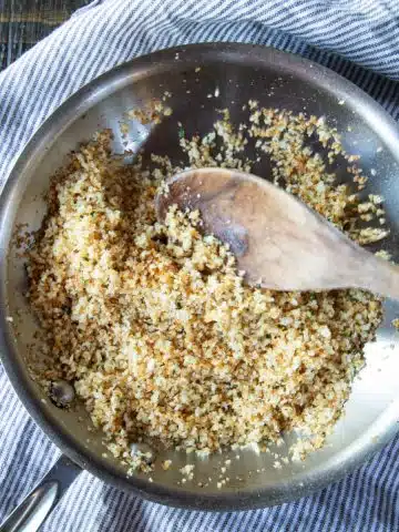 Breadcrumbs browned in a skillet with garlic and lemon zest, with a wooden spoon.