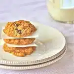 Three peanut butter, oatmeal cookies with chocolate chips stacked on top of each other on a plate.