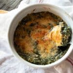 A serving bowl of creamed spinach topped with melted cheese.