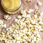 A bunch of popcorn scattered across some parchment paper, with a jar of nutritional yeast.