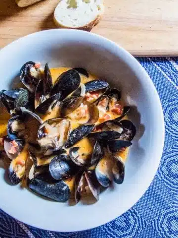A bowl of cooked mussels in a coconut curry sauce.