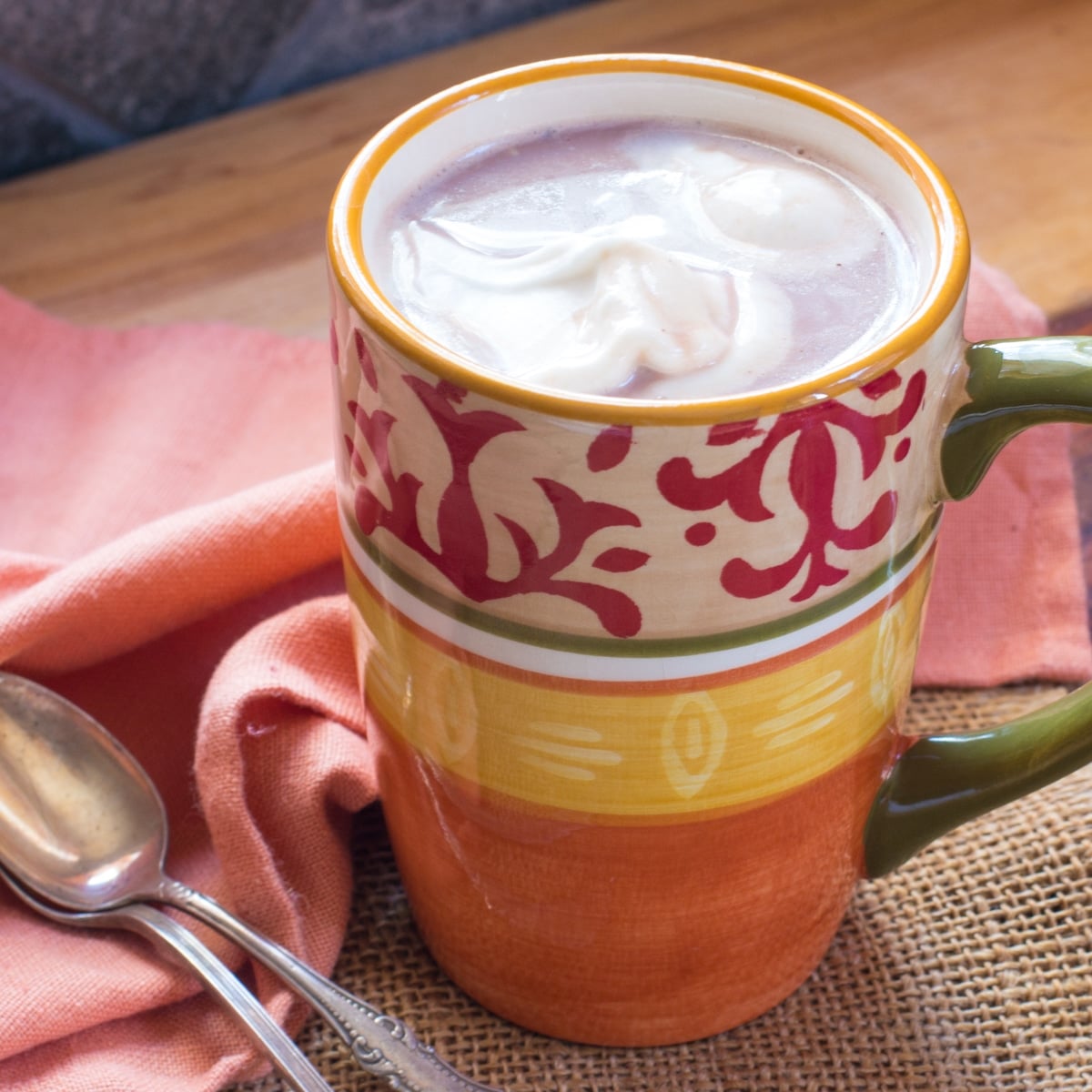 A cup of hot cocoa topped with coconut whipped cream, and 2 spoons.