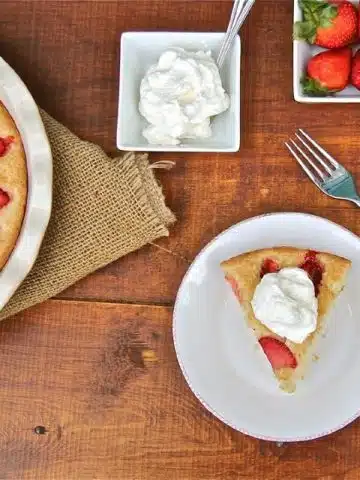 A piece of strawberry cake topped with whipped cream, and small dishes or strawberries and whipped cream.