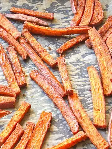Sweet potato fries on a parchment paper lined baking sheet, fresh from roasting in the oven.