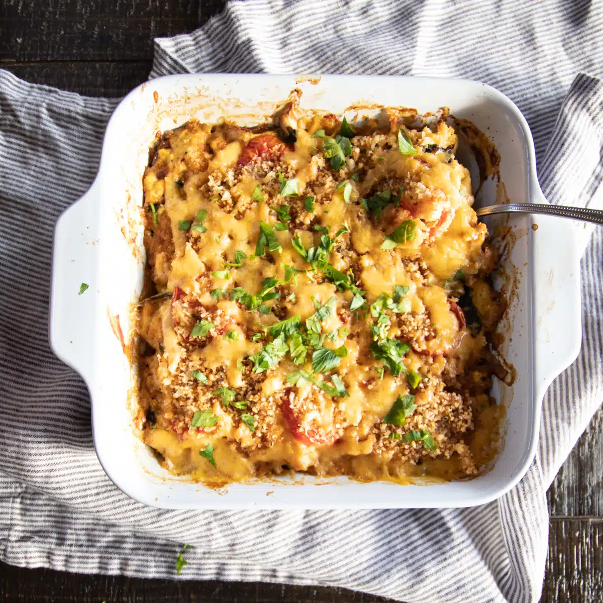 A cauliflower and tomato gratin topped with breadcrumbs, cheese, and chopped parsley in a small casserole dish.