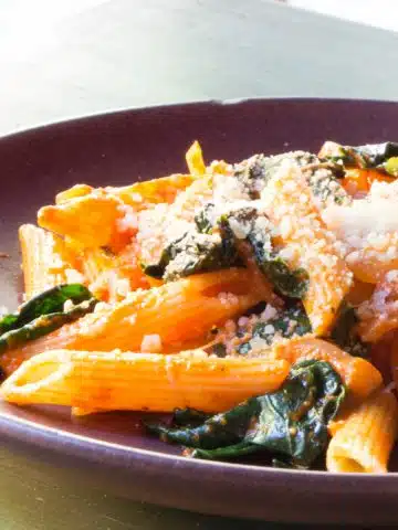 A plate of cooked penne pasta tossed in a roasted red pepper sauce, topped with Parmesan.