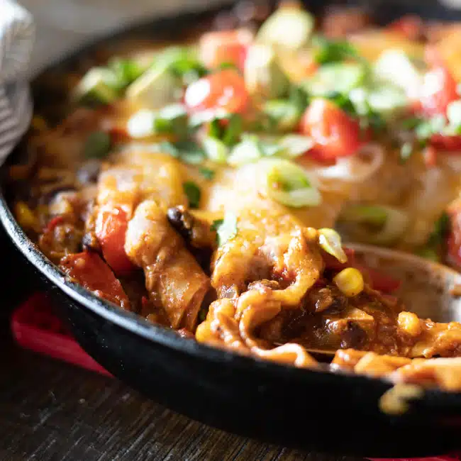 Close up of skillet enchiladas showing the cheesy topping, tortillas and filling.