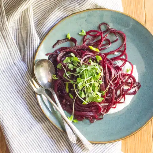 A plate of spiralized beets which look like beet spaghetti noodles. It's on whipped feta, and topped with sprouts.