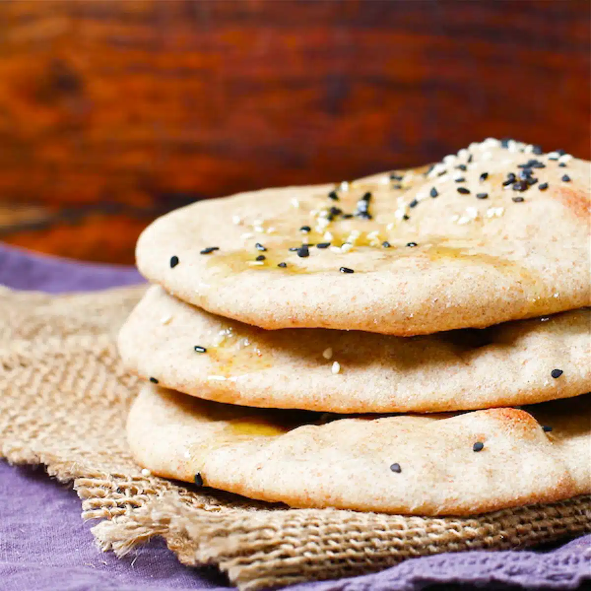 Three turkish flatbreads stacked, sprinkled with nigella seeds and drizzled with olive oil.