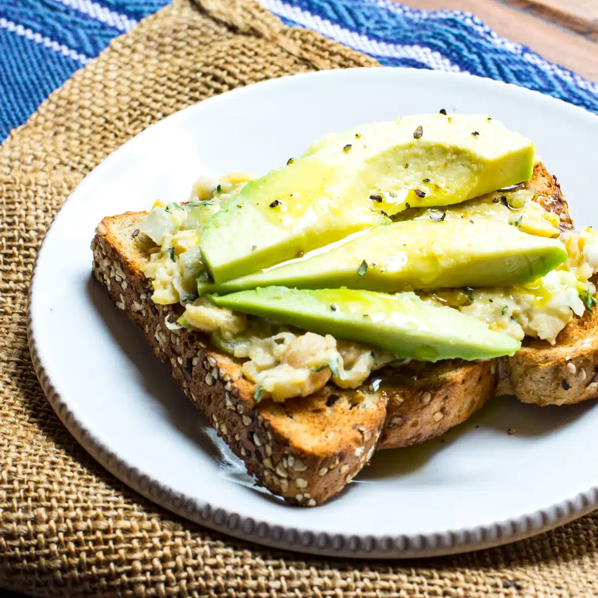 Chickpea salad spread on toast and topped with slices of avocado, a drizzle of olive oil and seasoned salt.