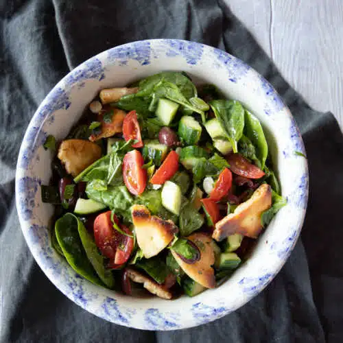 Bowl of fattoush salad of baby spinach, tomatoes, cucumber, crispy chickpeas and pita bread pieces.
