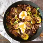 Seared Brussels sprouts in a skillet with caramelized red onions and two soft boiled eggs.
