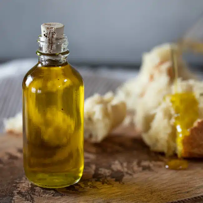 A small bottle of rosemary olive oil, with bread being drizzled with it in the background.