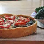 A cauliflower and kale tart with a cheddar cheese crust, topped with roasted tomatoes and cheese.