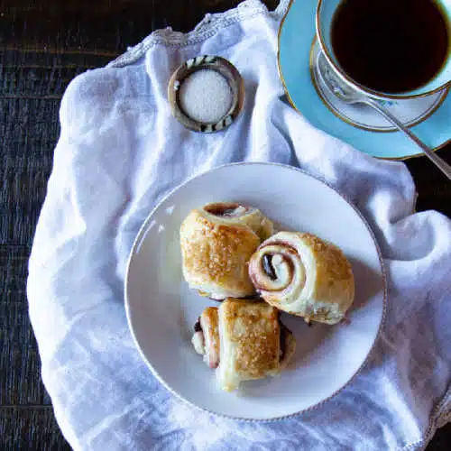 A small plate of three mini pain au chocolat with a cup of tea.