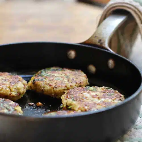 A skillet of patties made from cooked quinoa, baked potato, spinach and spices.