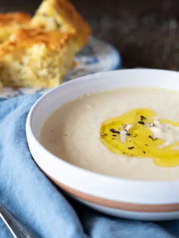 A bowl of cheesy cauliflower soup with rosemary oil drizzled on top.