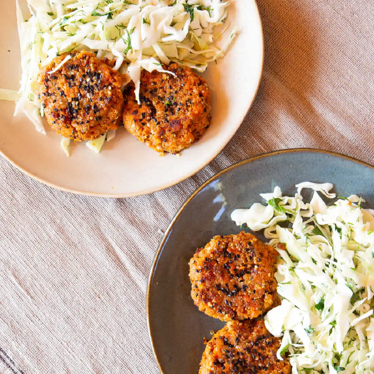 Two plates of sweet potato patties crusted with sesame seeds, with sides of coleslaw.